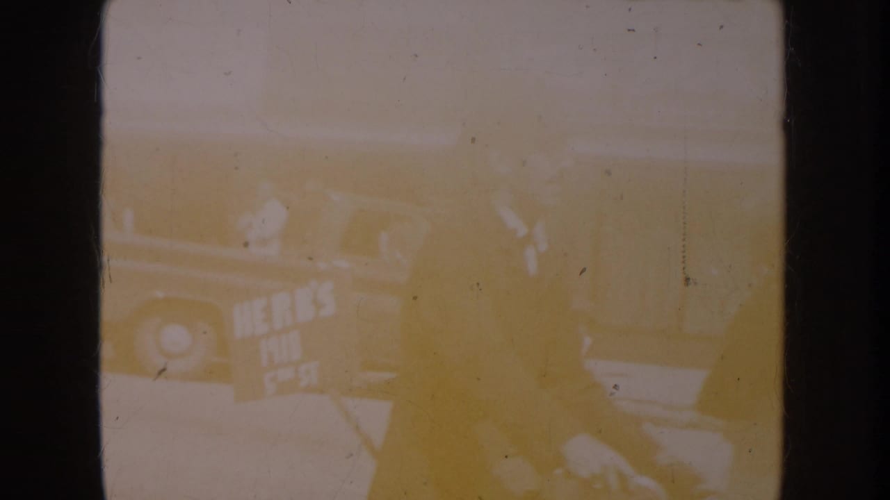 Overexposed opening frame from a circa-1955 8mm home movie; faint outlines suggest an outdoor street setting; detail lost to film burn.