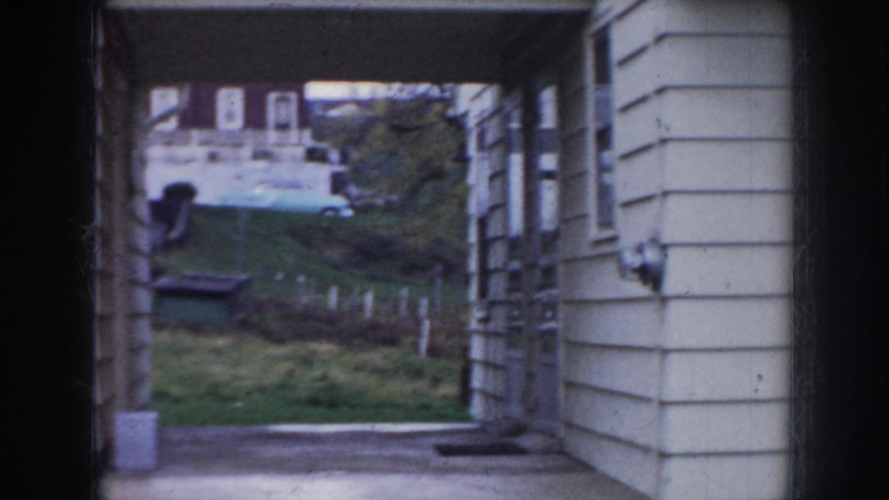 Low view through a porch opening toward a pale house exterior and small yard.
