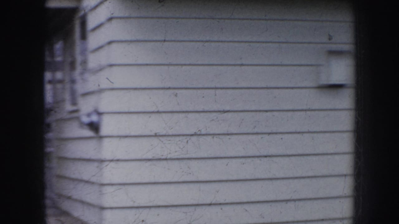 Close handheld view of pale horizontal siding and a dark porch post.