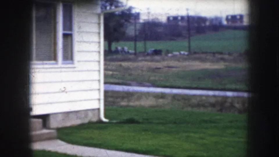 8mm home movie showing a cream-sided mid-century house exterior in rural Nebraska, circa 1956, with green lawn and open fields behind.