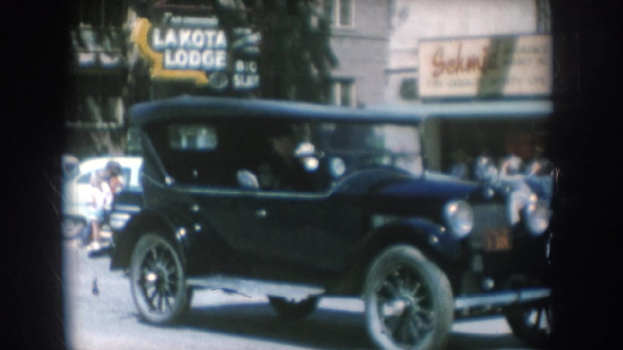 Black early-1920s-era sedan on a South Dakota small-town street in 1956, with LAKOTA LODGE sign clearly legible and spectators on the sidewalk.