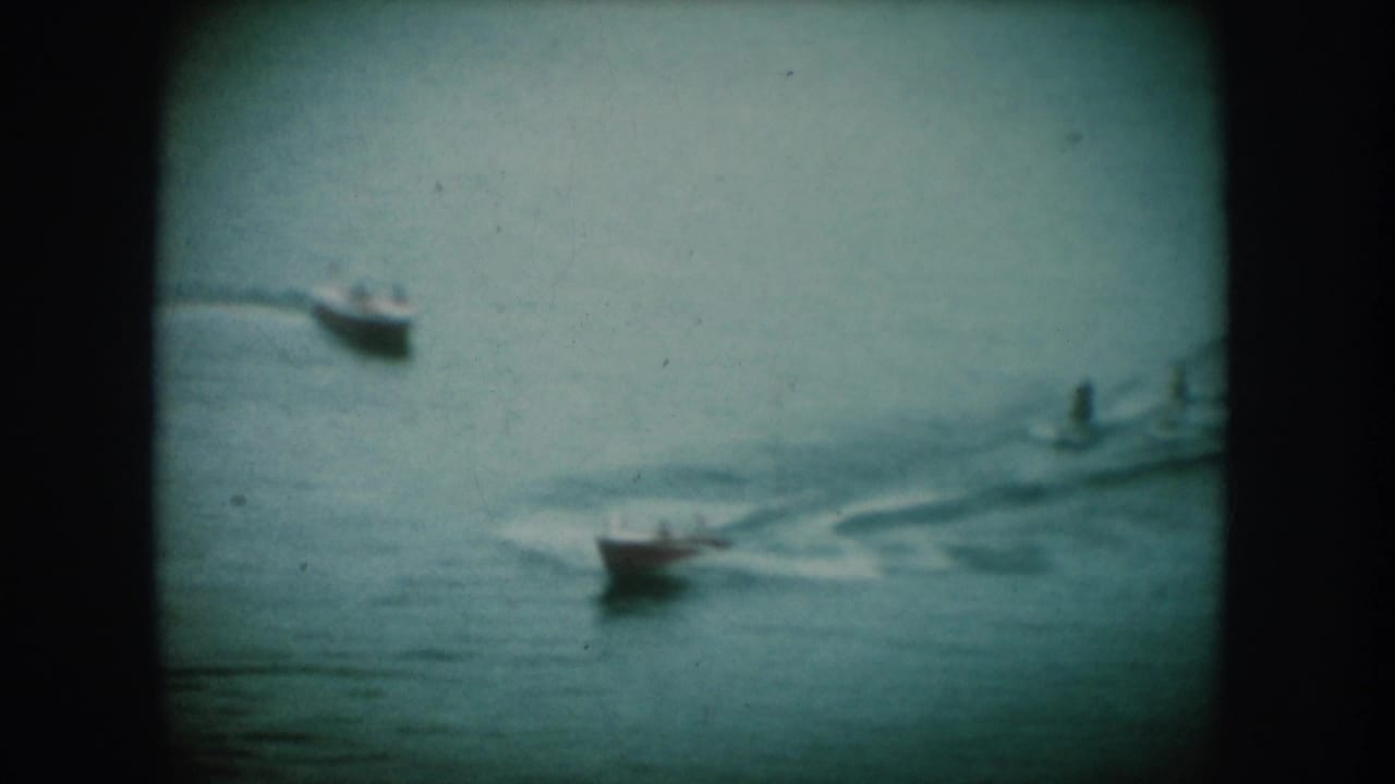 Two small motorboats on a calm lake leaving white wakes, shot on 8mm film with a cyan-green color tint.