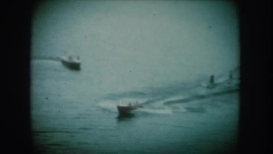 Two small motorboats cruise a calm lake in what appears to be mid-1950s South Dakota, captured on 8mm home movie film with a distinctive cyan color cast and rounded vignette border.