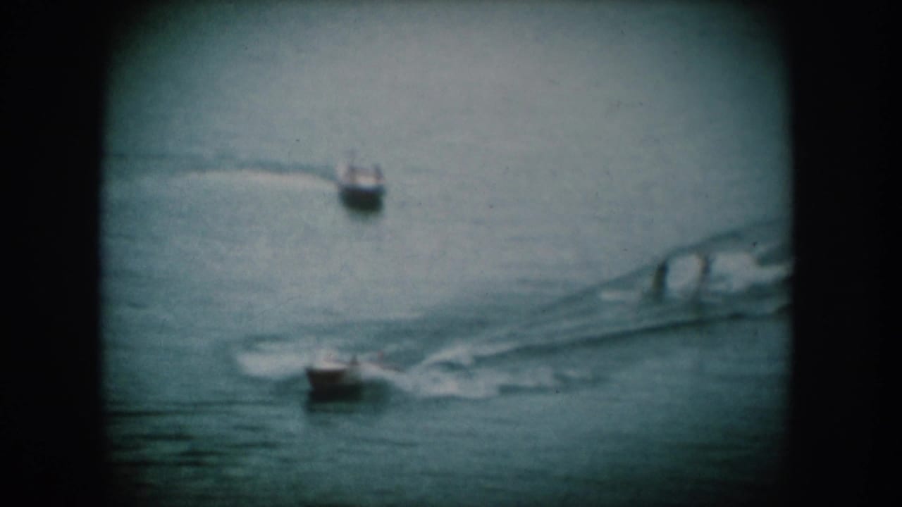 Two motorboats on a lake with visible white wakes; one boat in upper frame, one larger in center-right, on 8mm film.