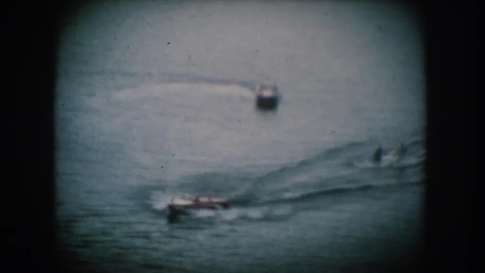 Two motorboats on a calm lake, the nearer vessel showing possible warm-colored hull detail, in what appears to be 1950s home movie footage from South Dakota.