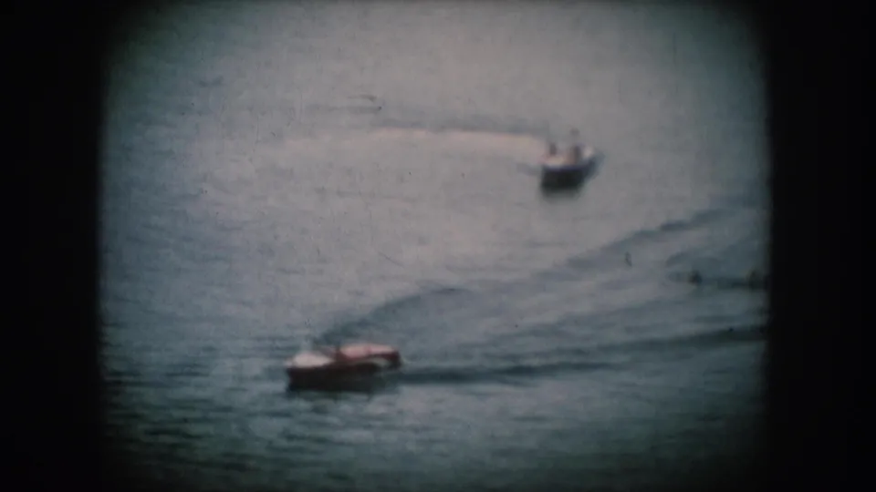 Two small motorboats cross a calm lake surface in what may be South Dakota, c. 1956; blue-tinted 8mm footage with rounded projector vignette.