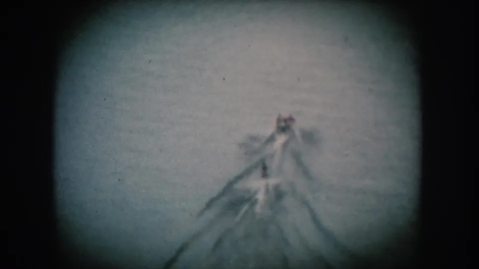A motorboat approaches the camera on an open lake, its wake fanning wide; blue-tinted 8mm home movie consistent with mid-1950s South Dakota leisure footage.