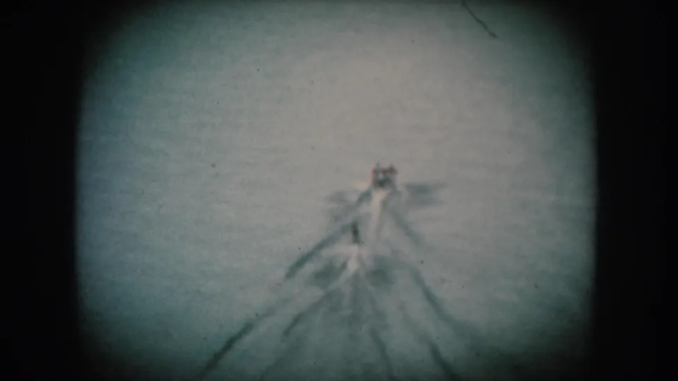 A motorboat traverses open lake water with a broad V-wake; blue-shifted 8mm reversal film consistent with mid-1950s American home movie production.