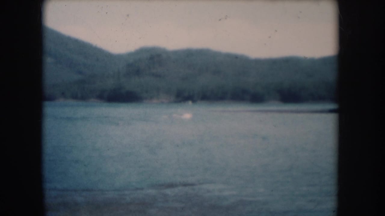Lake and forested hills in nearly identical composition to opening frame, on aged 8mm film.