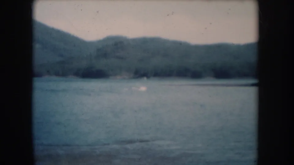 Lake with tree-covered hills in a 1956 8mm home movie attributed to South Dakota; composition nearly unchanged from opening.