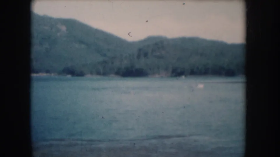 Prominent forested hillside over lake foreground in a 1956 8mm home movie attributed to South Dakota.