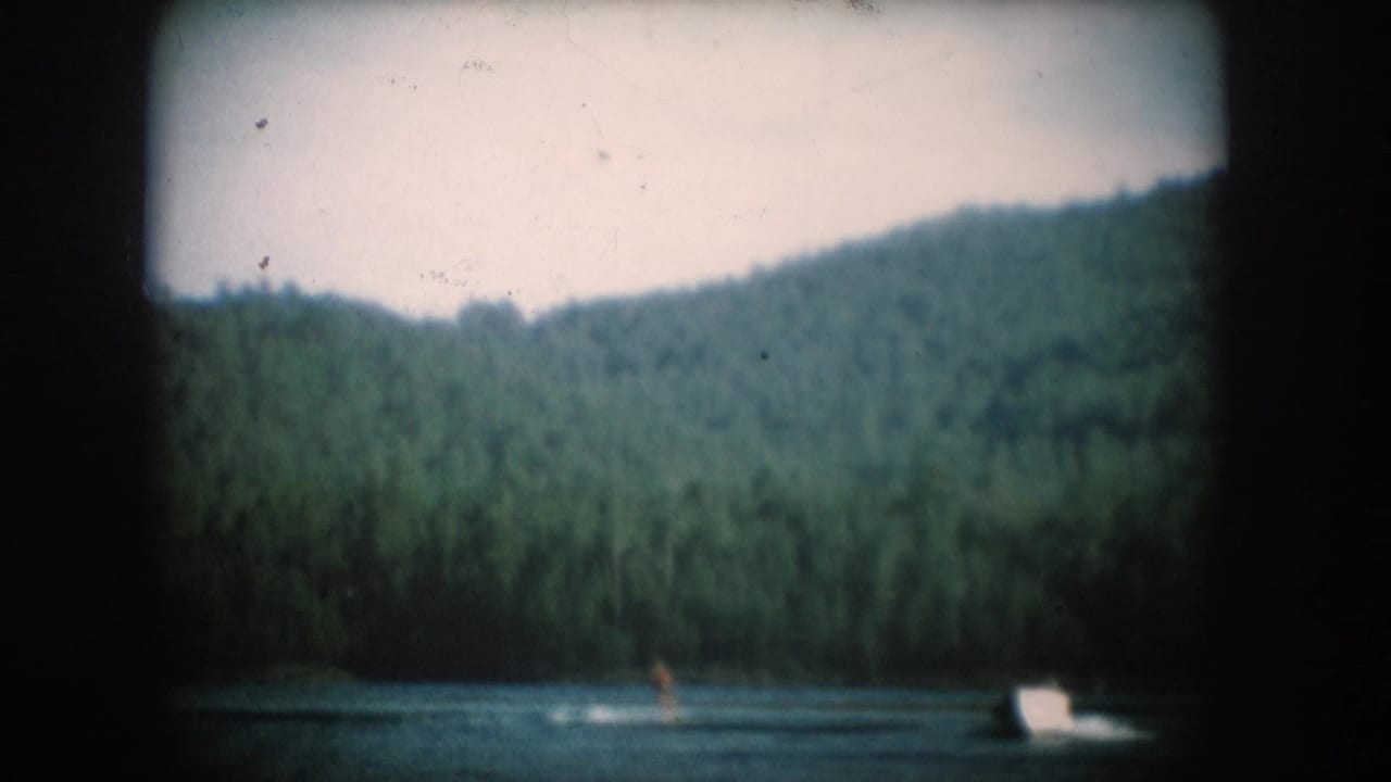Motorboat towing a water-skier across a South Dakota lake, conifer hillside behind, circa 1956, 8mm home movie with vignetting.