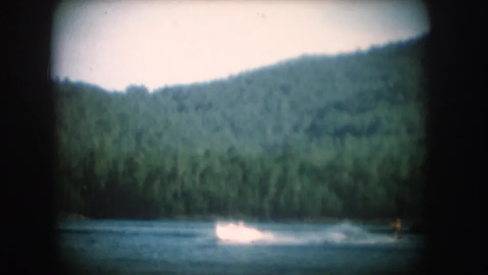 Motorboat wake and skier on a South Dakota lake, heavily forested hillside rising behind, circa 1956, 8mm home movie.