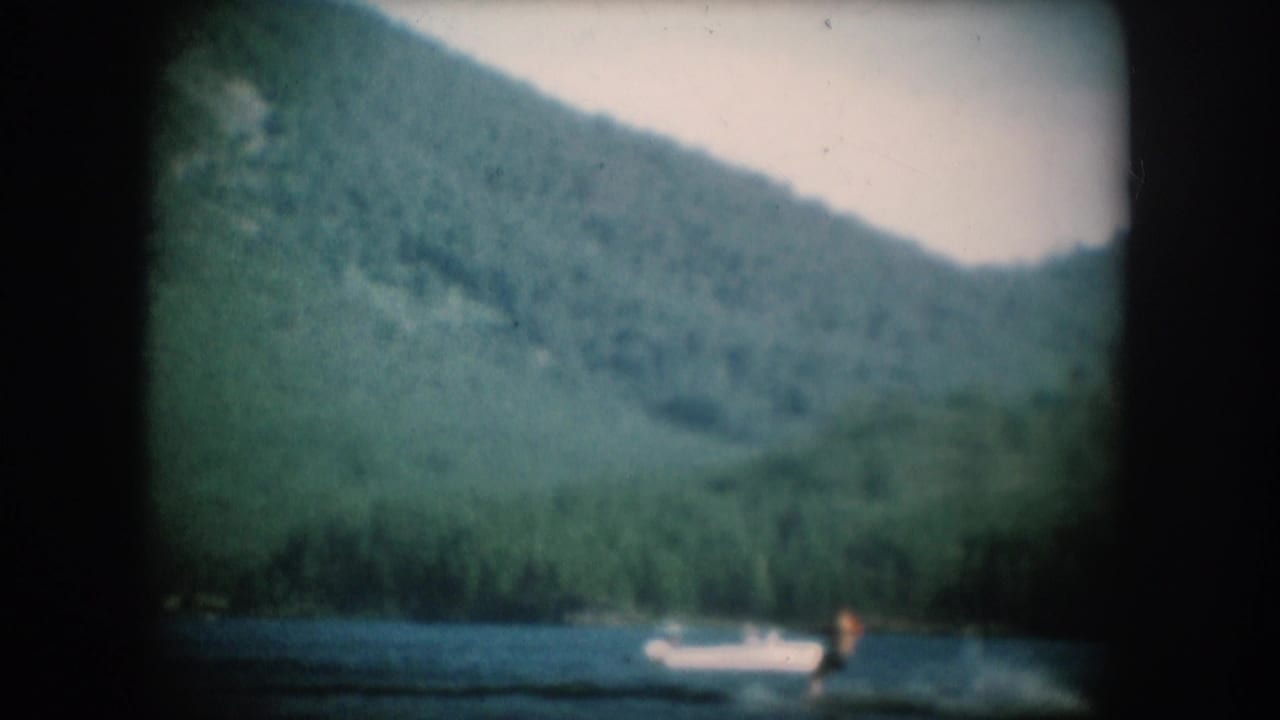 Forested mountain ridge above a lake with a white motorboat and distant figure visible on the water.