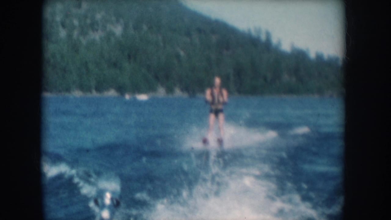 Closing frame of an 8mm clip showing a water skier on a forested lake consistent with mid-1950s recreational home movie footage, metadata-attributed to South Dakota, USA.