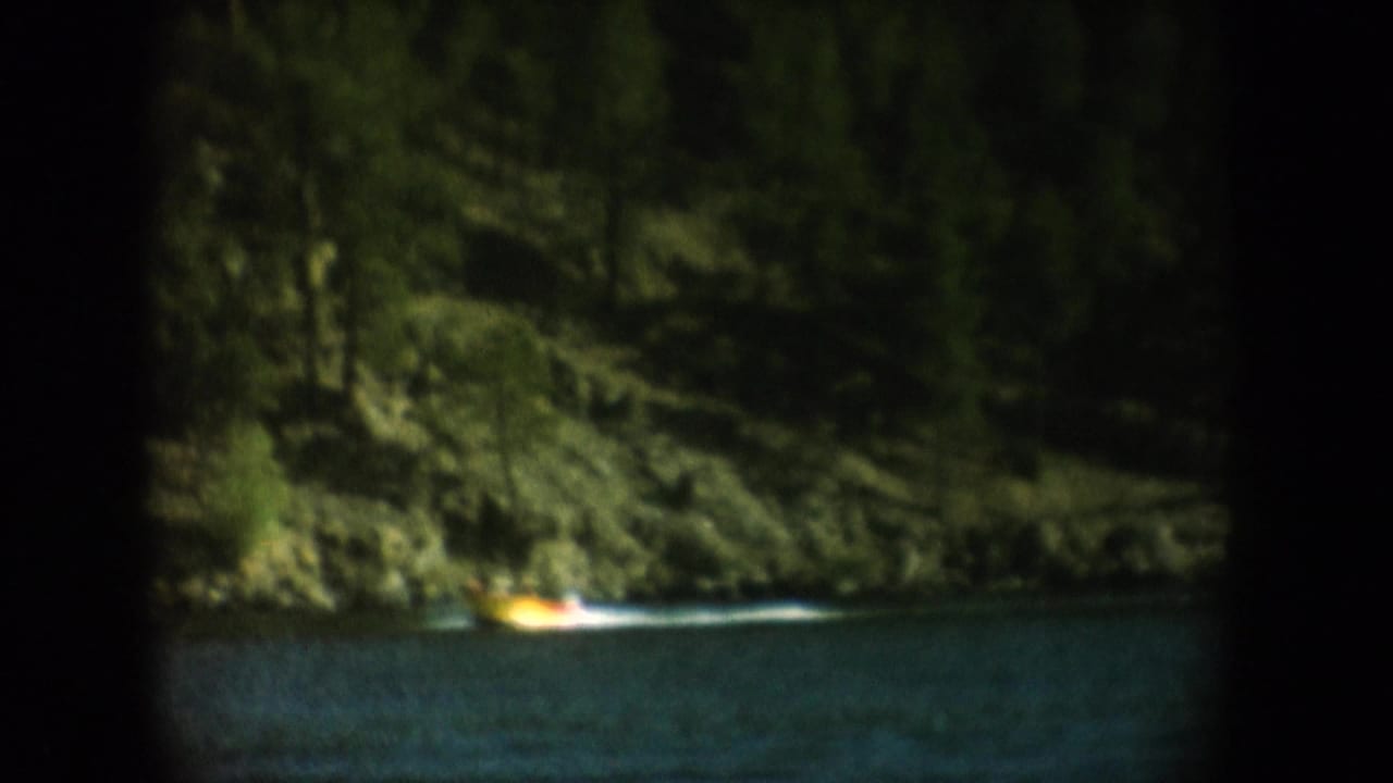 Yellow tow boat crossing a forested lake in South Dakota, circa 1956, shot on 8mm home movie film