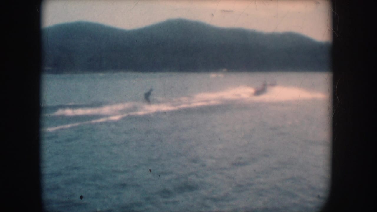 Water skier on a lake, warm pink-shifted 8mm color, wooded hills visible in background