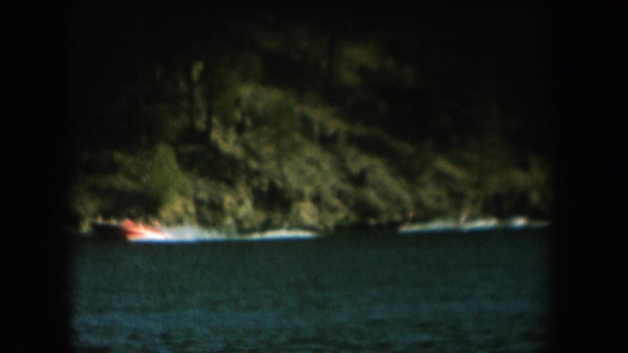 Continued low-light 8mm footage: forested cliff and dark water with orange boat light, same reel as daytime water skiing, c. 1956