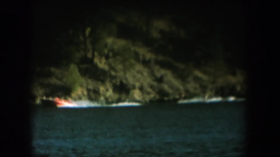 Continued low-light 8mm footage: forested cliff and dark water with orange boat light, same reel as daytime water skiing, c. 1956