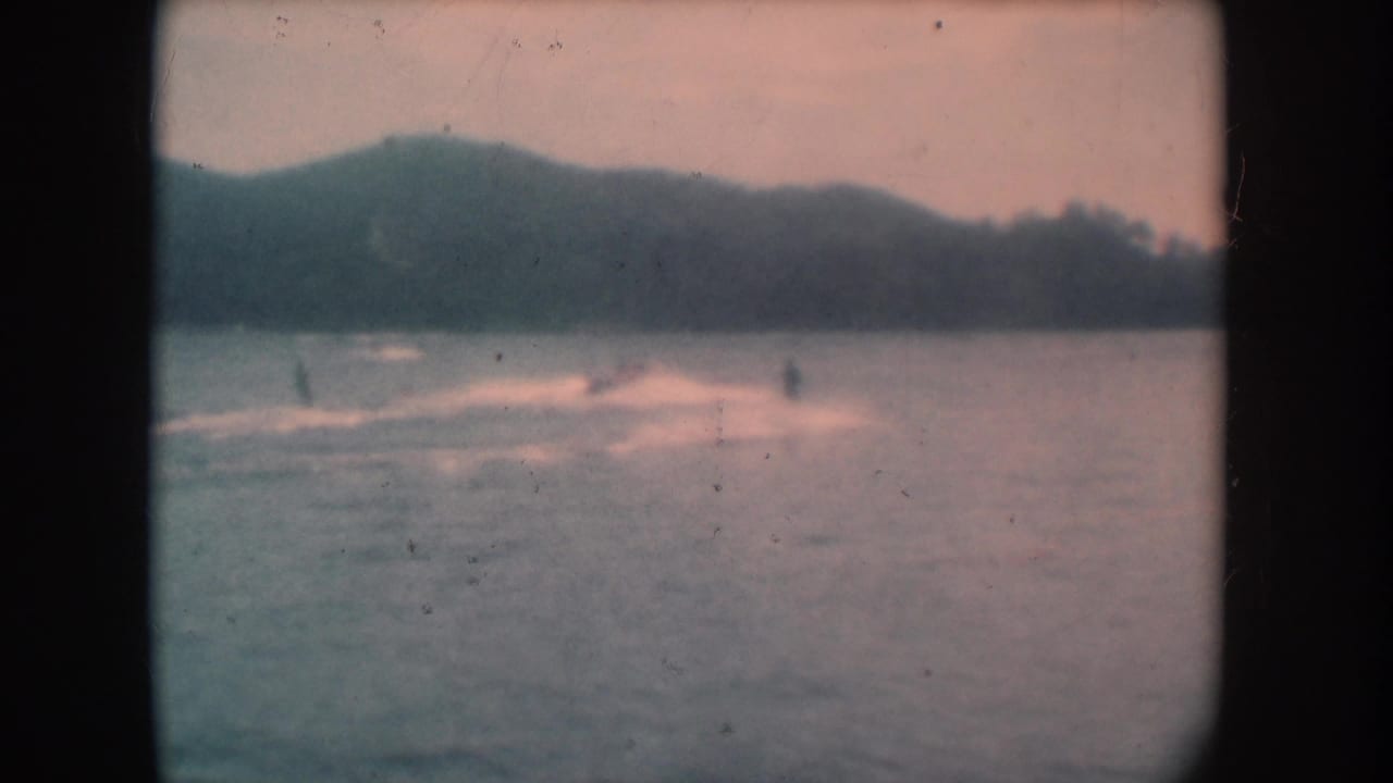 Lake scene with rolling hills, faded pink emulsion, distant figure on water, 8mm film grain
