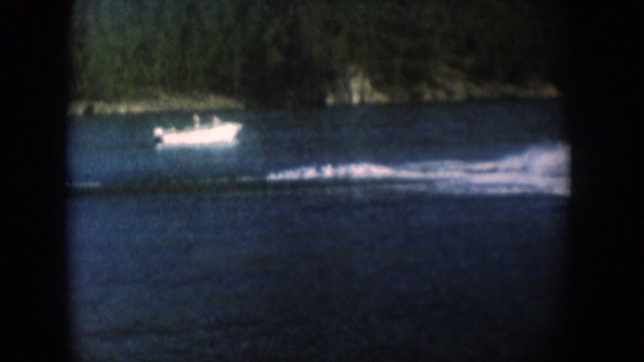 Light-colored motorboat crossing a blue lake with a forested shoreline; strong color fade and heavy vignetting.