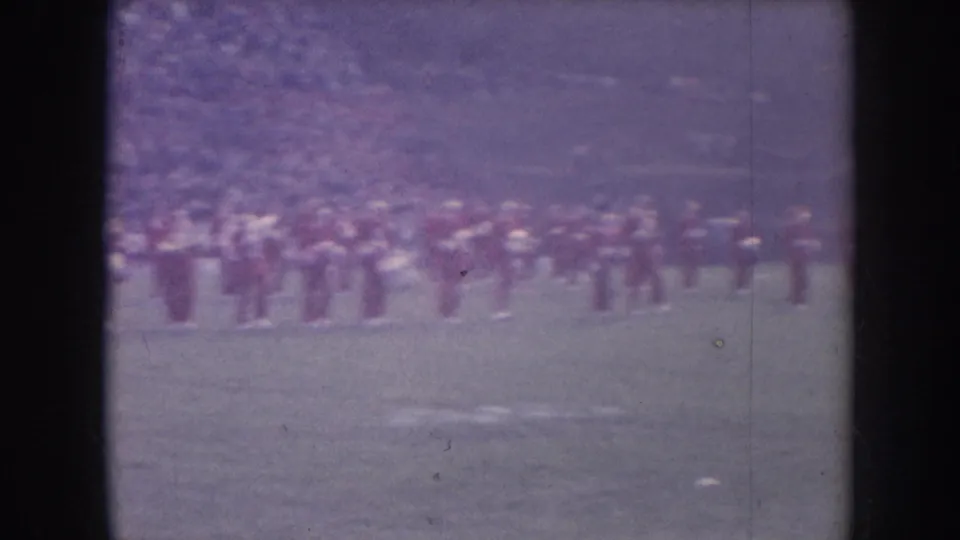 8mm frame with strong purple color drift showing band formation on football field; exemplifies spectral degradation common in aged mid-century color film stock.