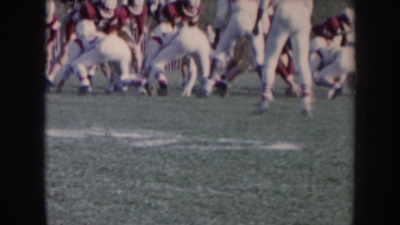 Football players in white and dark uniforms crouched at the line of scrimmage on a grass field.