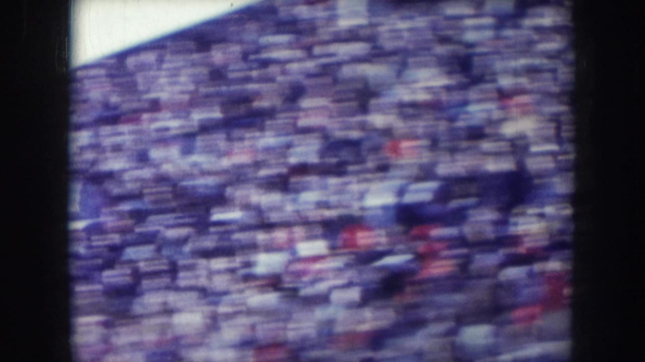 Blurred 8mm shot of a packed stadium crowd filling the stands, captured during a pan.