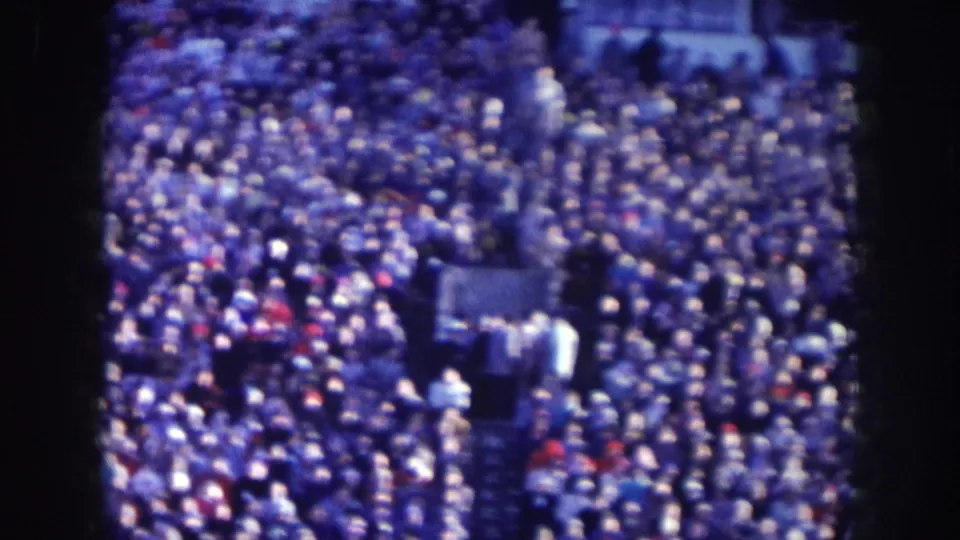 Overhead 8mm film view of a densely packed crowd at what appears to be a public gathering in Nebraska, circa 1957, with heavy blue cast and film grain.