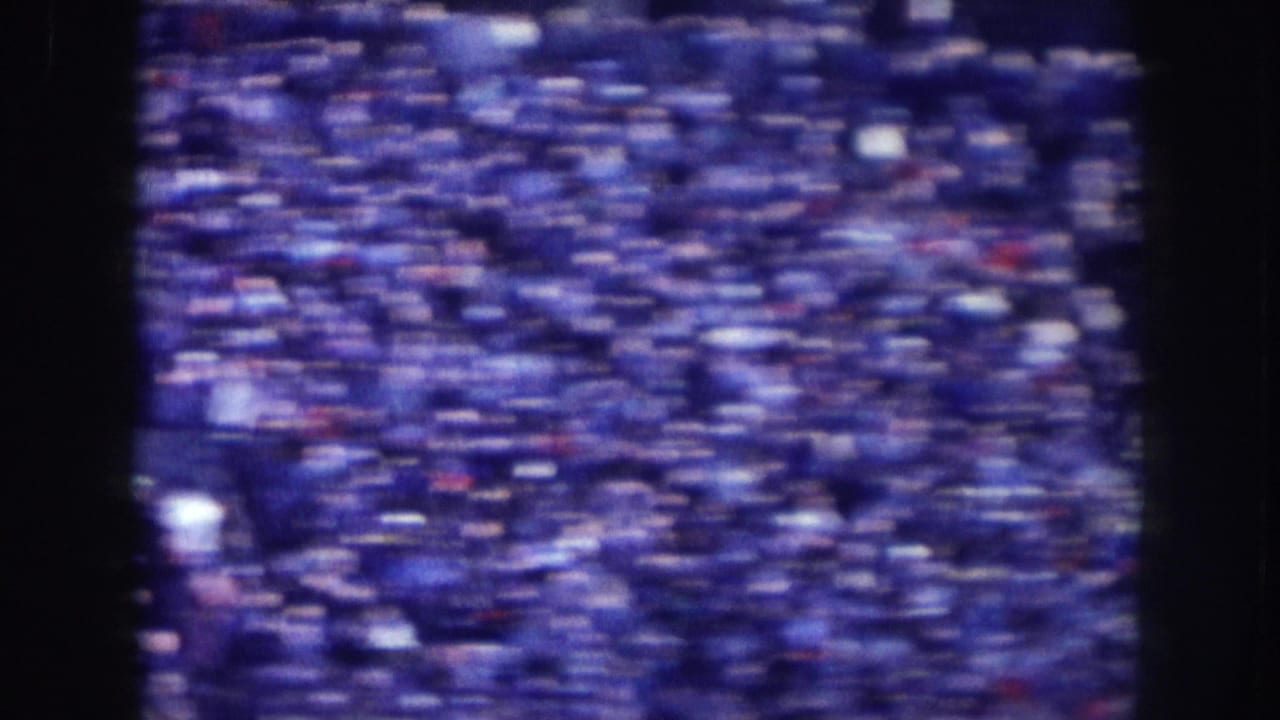 Tightly packed crowd viewed from elevation, possibly Nebraska circa 1957; heavy 8mm grain and blue color shift from aged film stock throughout.