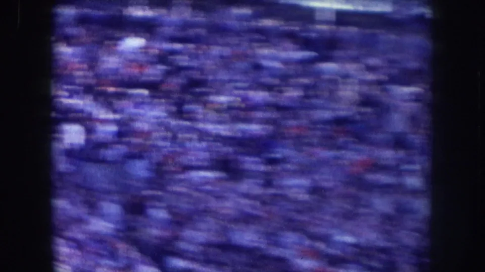 Camera pan across crowd produces significant motion blur throughout frame; blue-cast 8mm film from what may be a Nebraska public event, circa 1957.