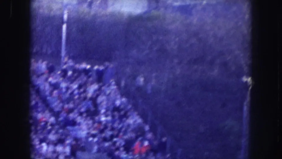 Crowd gathered along what may be a parade route or cleared street, with a vertical pole visible; elevated 8mm view with blue cast and film grain, possibly Nebraska circa 1957.