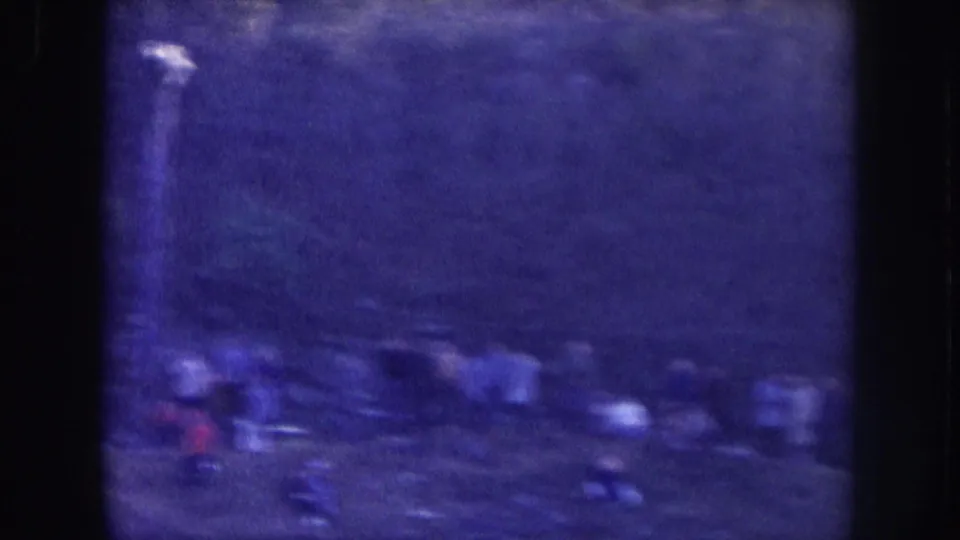 Several blurred figures outdoors, filmed on 8mm circa 1957 in Nebraska; deep blue-purple color shift and heavy grain render detail indistinct.