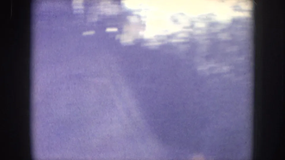Dense smoke plume rising against a blown-out sky, filmed on 8mm circa 1957; heavy grain and purple-lavender color cast typical of aged amateur film stock.