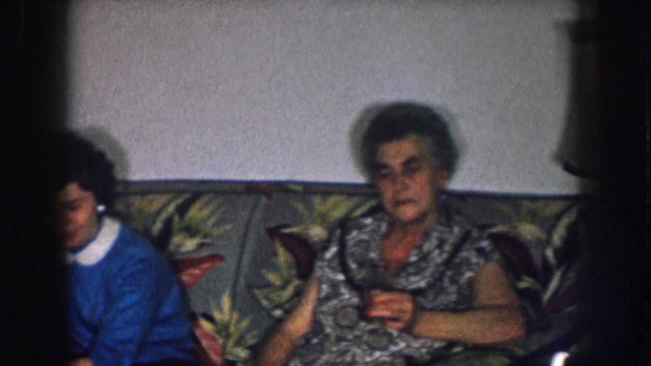 Older woman on floral couch with a younger woman in a blue sweater leaning in beside her; brass lamp visible at right.