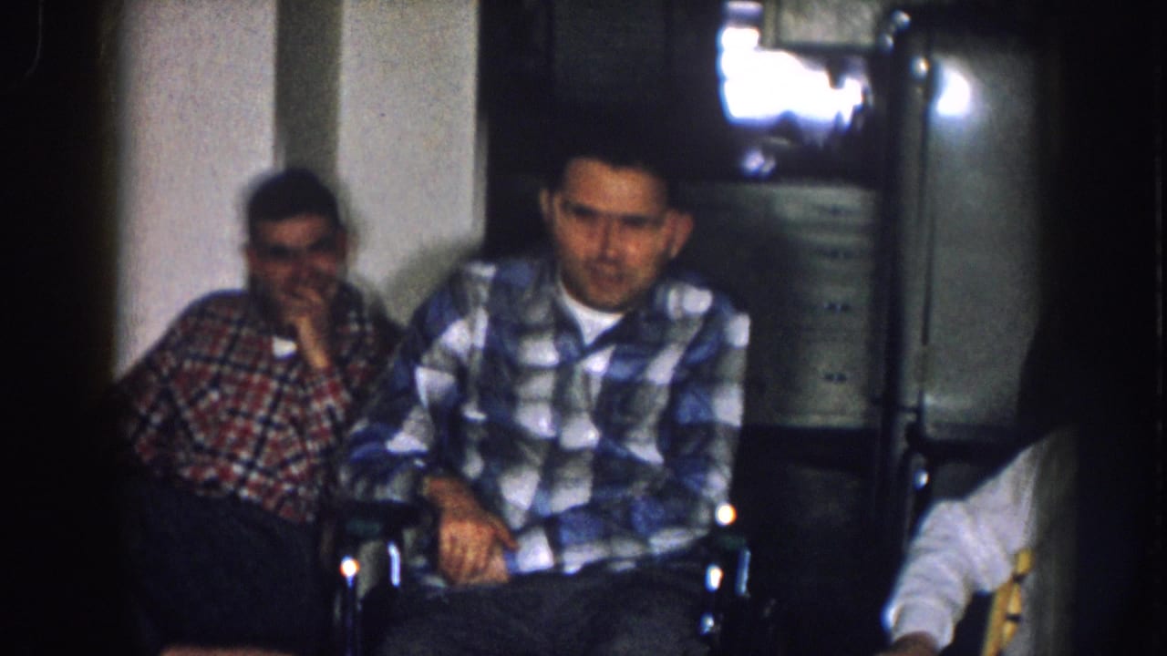 Two men in plaid shirts seated in a dim domestic room, with a boxy early television set visible in the upper background.