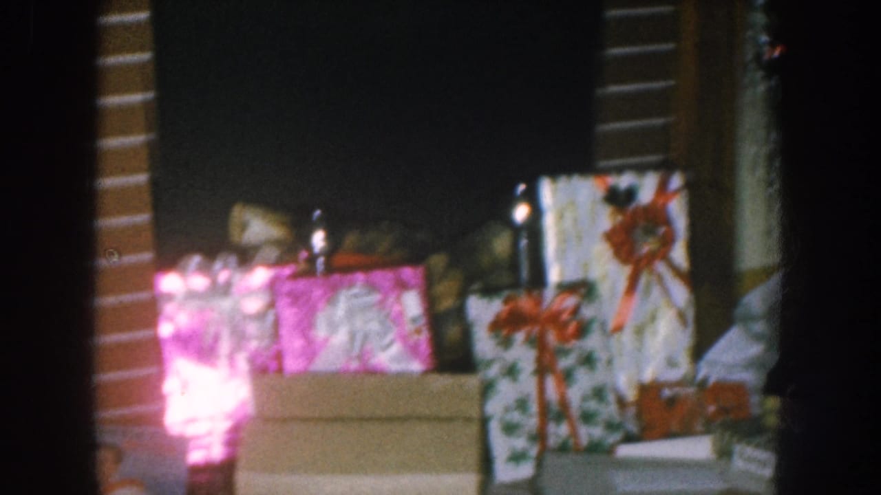Wrapped Christmas gift boxes with red ribbon bows on a surface, a bright pink-magenta glow at left, dark interior background with wood paneling.