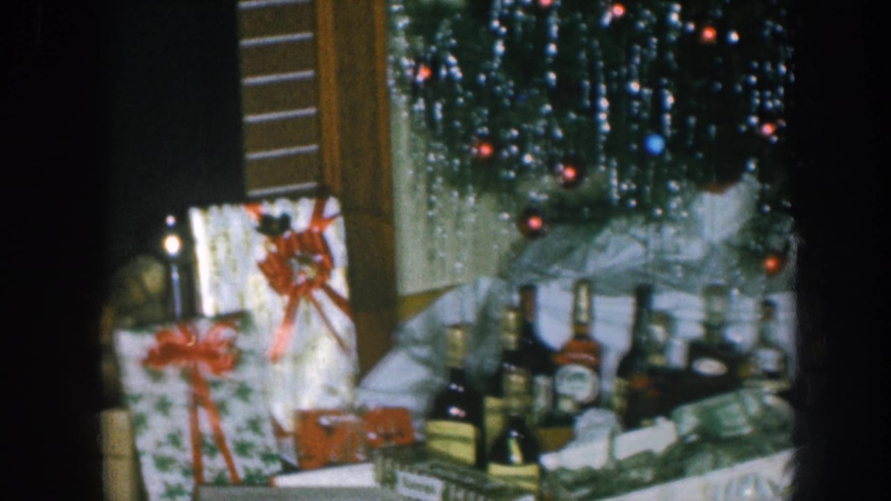 1957 Nebraska home movie: pan revealing wrapped gifts, red ribbon bows, spirit bottles, and the base of a silver-tinsel Christmas tree strung with colored fairy lights.