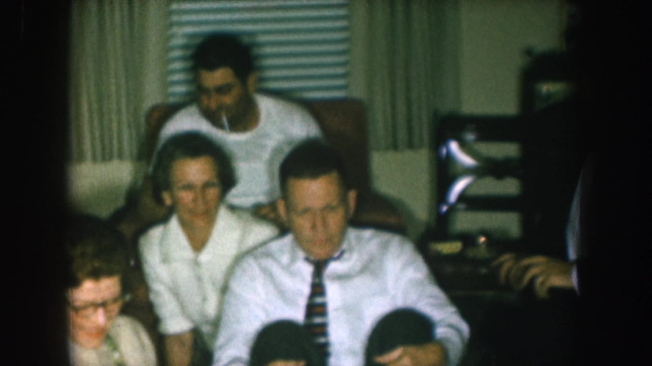 Several adults sit near a television set in a living room during a Christmas gathering.
