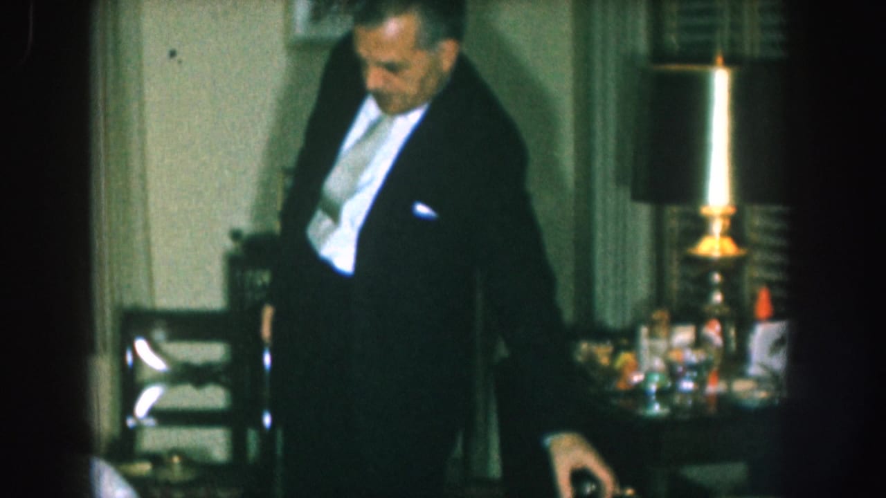Man in dark formal jacket standing at a party table with glassware and a lit brass candlestick, 8mm home movie, likely Nebraska, 1957.