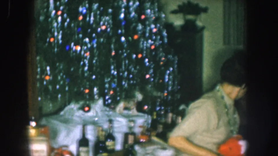 Aluminum tinsel Christmas tree decorated with multicolored lights beside a party table with liquor bottles and wrapped gifts, c. 1957 Nebraska.