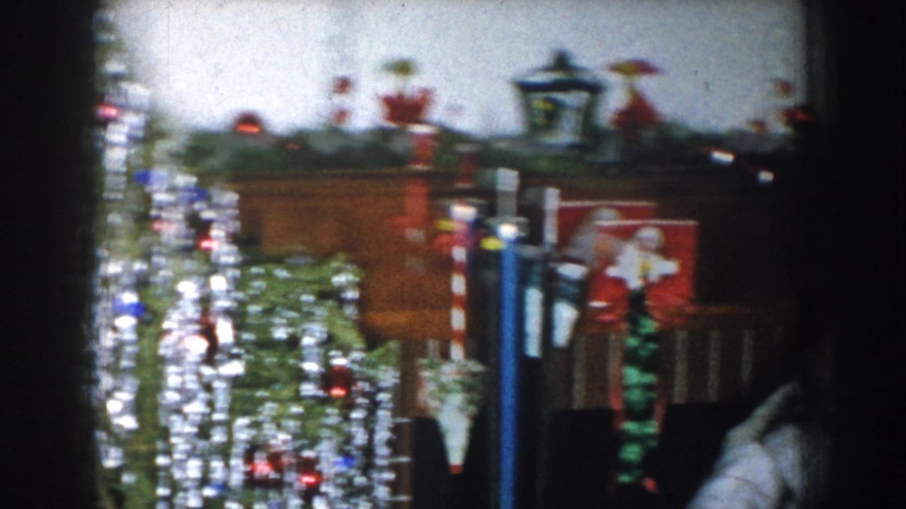 Overexposed pan shot of a decorated Christmas tree covered in multicolored lights; Santa figurine or decoration visible at right edge.