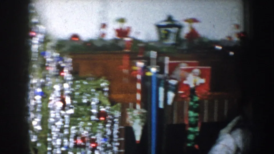 Camera pan across a heavily lit Christmas tree with multicolored lights, Nebraska USA, circa 1957; Santa decoration visible at frame right.