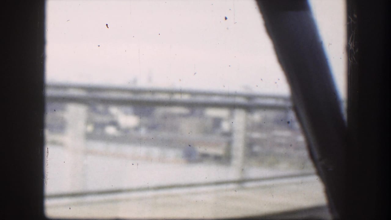 8mm home-movie frame shot from a moving vehicle through a car window, looking up at a highway overpass consistent with late 1950s road travel.