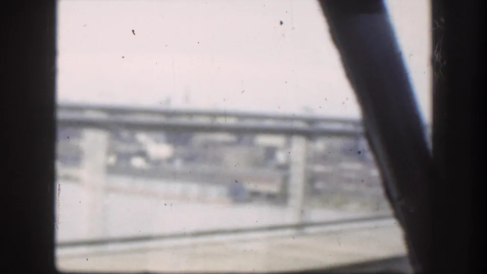 8mm home-movie frame shot from a moving vehicle through a car window, looking up at a highway overpass consistent with late 1950s road travel.