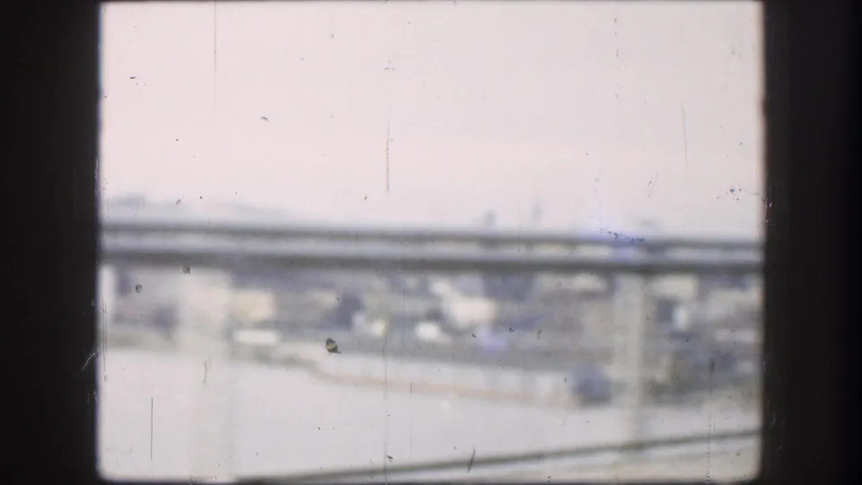 8mm frame from a moving vehicle looking at a highway overpass, with hazy sky and blurred structural elements, consistent with 1950s American road travel.