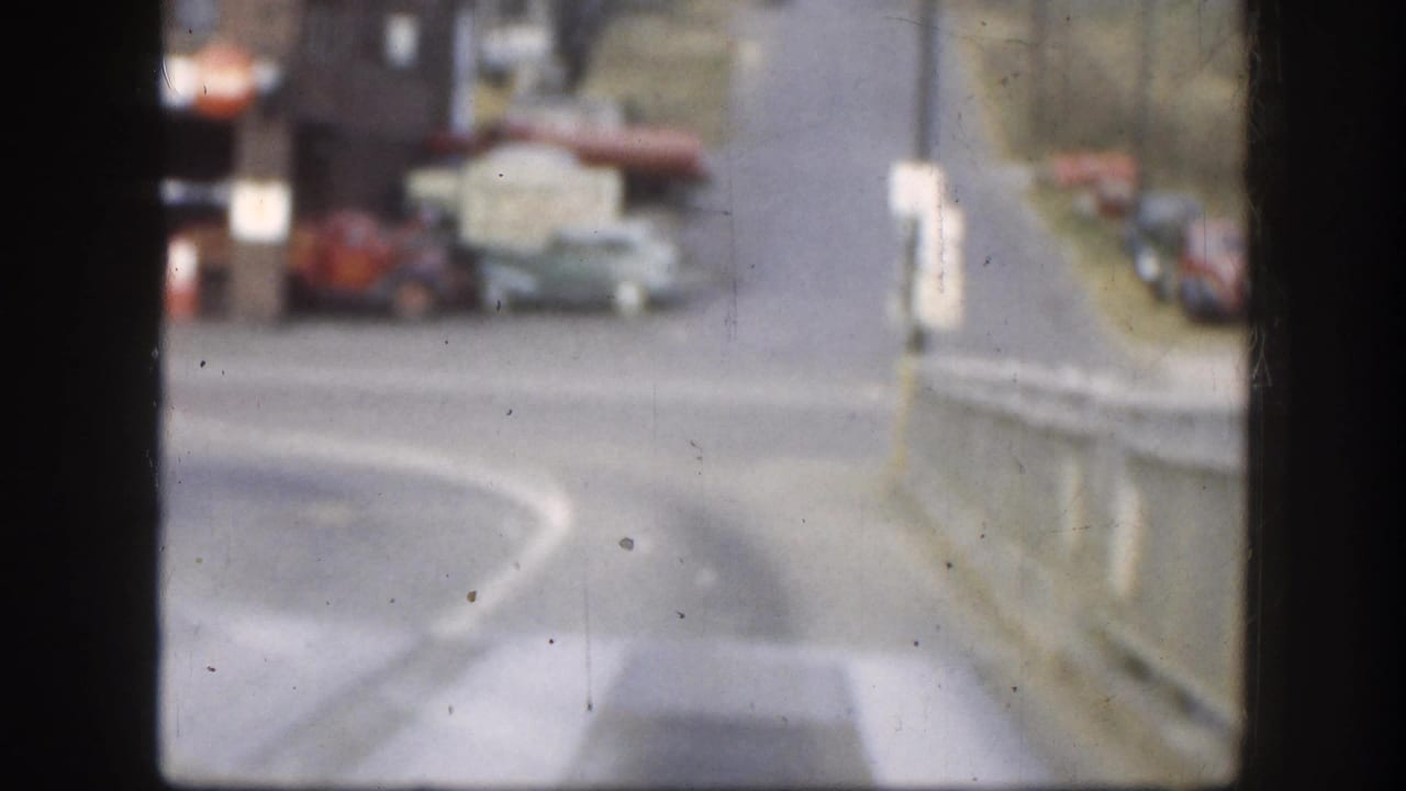 Soft-focus 8mm color street scene from Kansas, circa 1958, showing period automobiles on a two-lane road with buildings in the background.