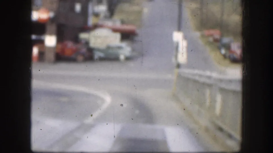 Soft-focus 8mm color street scene from Kansas, circa 1958, showing period automobiles on a two-lane road with buildings in the background.