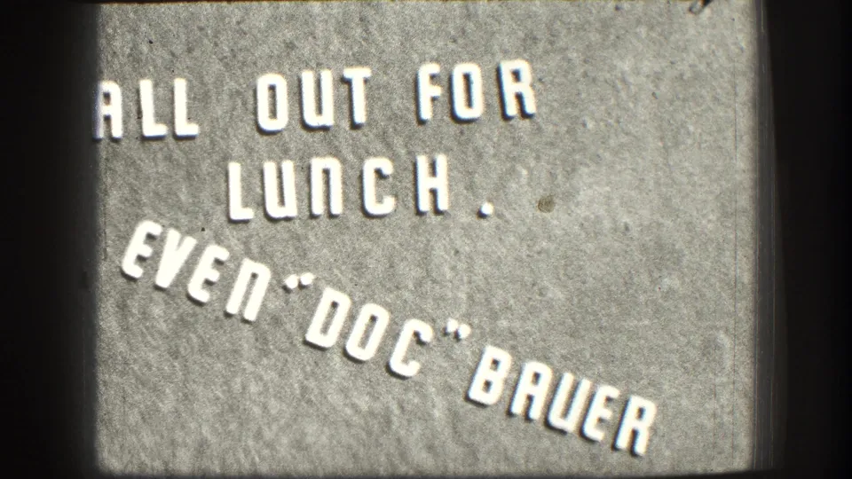8mm color close-up of informal business lunch sign in white stenciled lettering on textured concrete, Kansas, circa 1958.