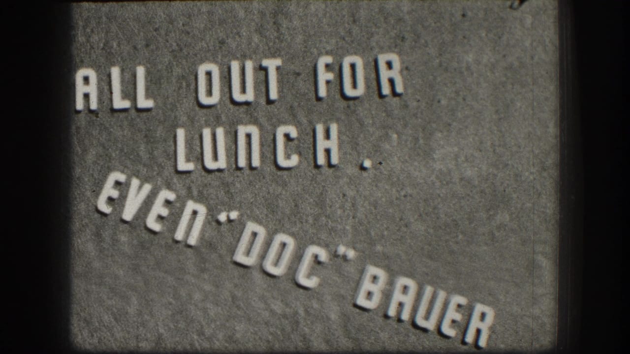 8mm home movie intertitle circa 1958 with embossed-style text reading 'ALL OUT FOR LUNCH. EVEN DOC BAUER' on a gray textured background.